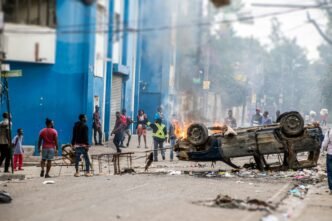 Des manifestants expriment leur colère en brûlant une voiture devant un poste de police en Haïti. Les tensions s'intensifient dans le pays, reflétant les défis auxquels la société haïtienne est confrontée. Crédit Photo : Carlin Trezil